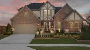 Two-story home design features light brown brick and gray toned cedar trim. Lush landscacping and a cozy porch at the front of the home.