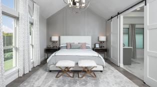 A spacious gray and white bedroom with high ceilings and a comfortable king-sized bed. 